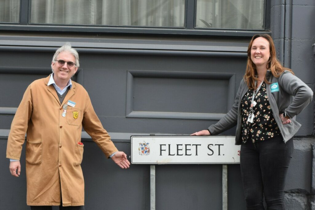 two people pointing at a road sign that says "Fleet Street".